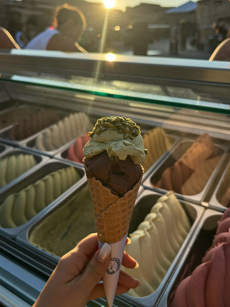 Pistachio and chocolate gelato cone held in front of the display trays